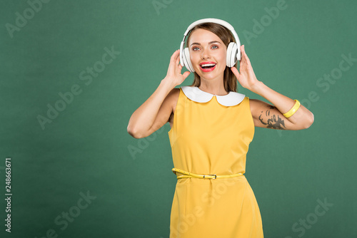 beautiful happy woman in yellow dress and headphones isolated on green with copy space