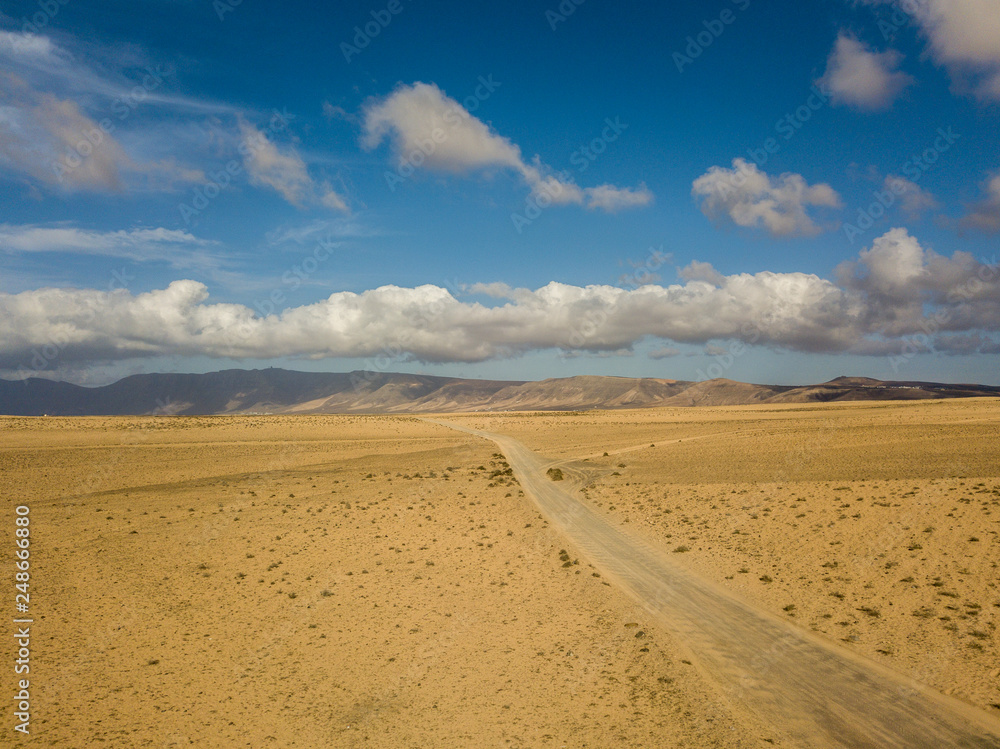 Aerial view of a desert landscape on the island of Lanzarote, Canary Islands, Spain. Road that crosses a desert. Tongue of black asphalt cutting a desert land. Reliefs on the horizon. Volcanoes