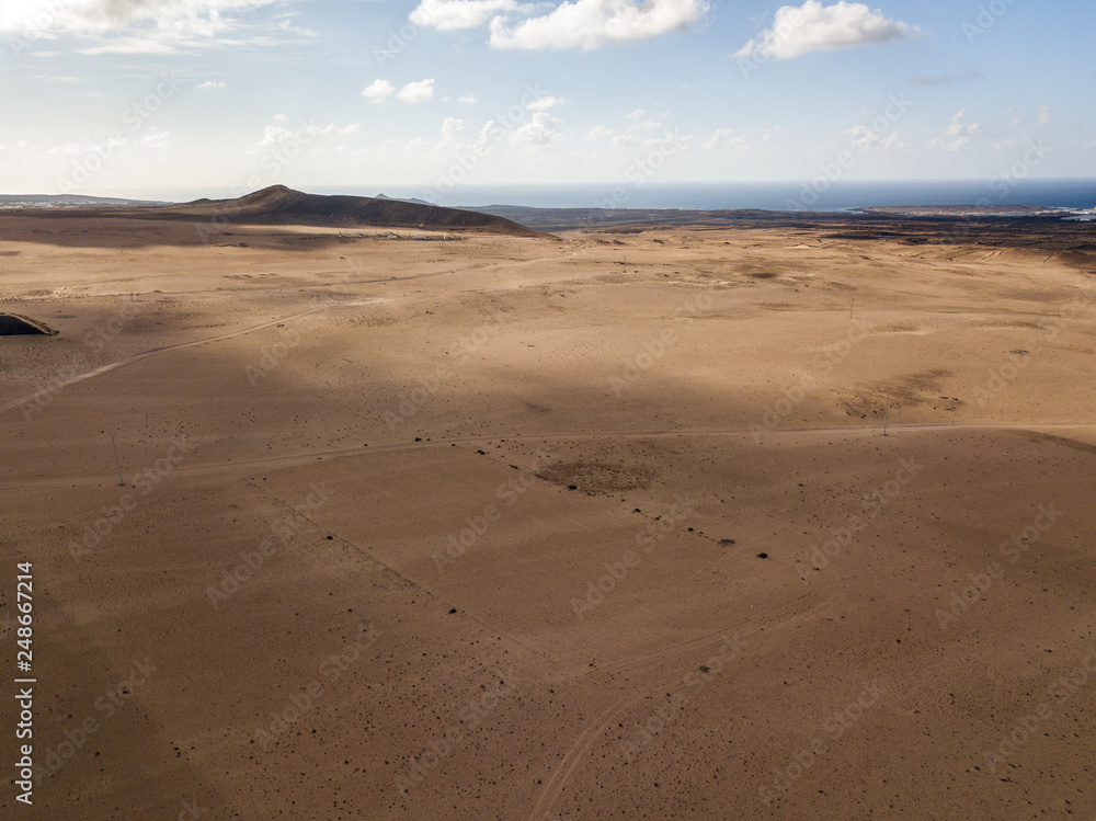 Aerial view of a desert landscape on the island of Lanzarote, Canary Islands, Spain. Road that crosses a desert. Tongue of black asphalt cutting a desert land. Reliefs on the horizon. Volcanoes