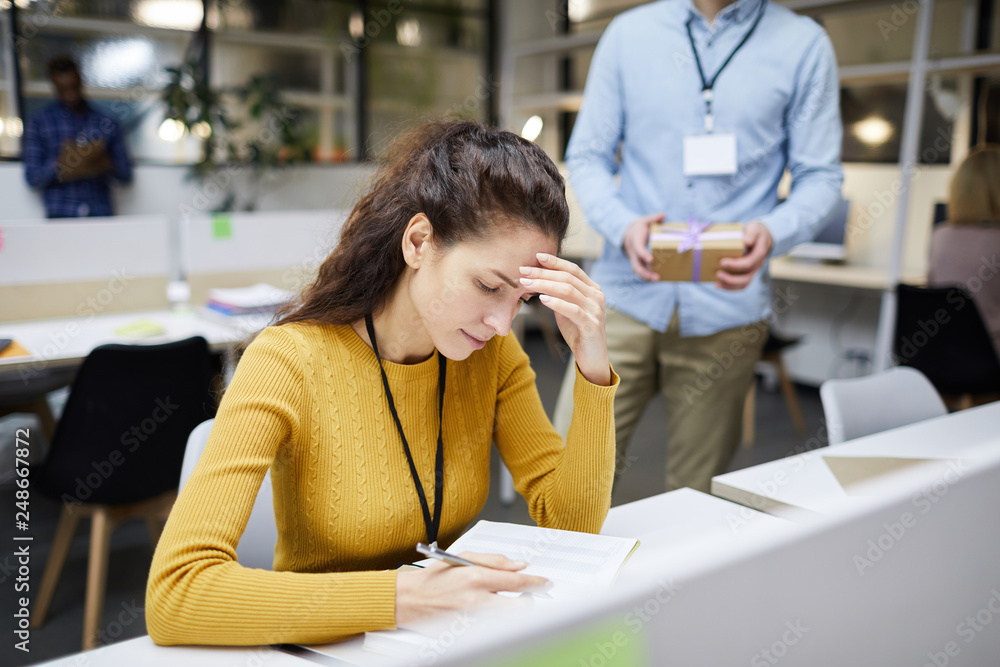 Serious upset young woman tired from work sitting at desk in office and rubbing forehead while reading notes in diary Serious upset young woman tired from work sitting at desk in office and rubbing forehead while reading notes in diary