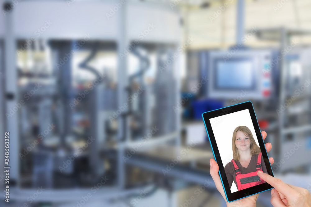 Female is using the smart phone with photo of female worker in overall on the screen. Blurred automatic production line is in the background. Female is using the smart phone with photo of female worker in overall on the screen. Blurred automatic production line is in the background.