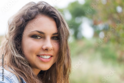 Portrait of smiling tanned longhair brunette teenage girl with white teeth outdoors closeup. © frank11