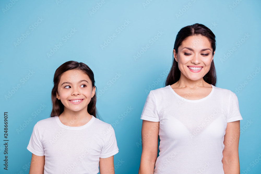 Close up photo amazing pretty two people brown haired mum and small daughter standing straight looking side each other cunning wearing white t-shirts isolated on bright blue background Close up photo amazing pretty two people brown haired mum and small daughter standing straight looking side each other cunning wearing white t-shirts isolated on bright blue background