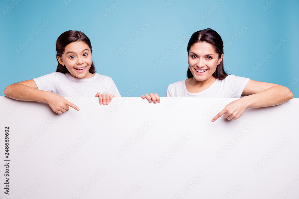 Close up photo beautiful two people brown haired mom little daughter finger point on signboard poster arms hold white poster sale discount wearing t-shirts isolated bright blue background Close up photo beautiful two people brown haired mom little daughter finger point on signboard poster arms hold white poster sale discount wearing t-shirts isolated bright blue background