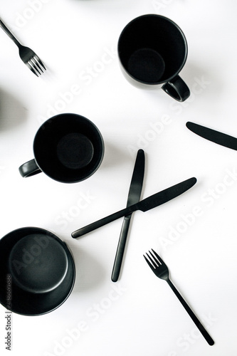 Black kitchenware: forks, knifes, mugs, bowls on white background. Flatlay, top view modern kitchen concept.