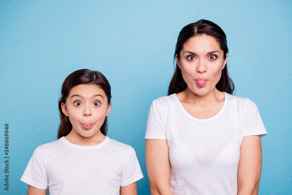 Close up photo beautiful two people brown haired mom little daughter friends look silly eyes opened tongue out of mouth playing fooling around wear white t-shirts isolated bright blue background Close up photo beautiful two people brown haired mom little daughter friends look silly eyes opened tongue out of mouth playing fooling around wear white t-shirts isolated bright blue background