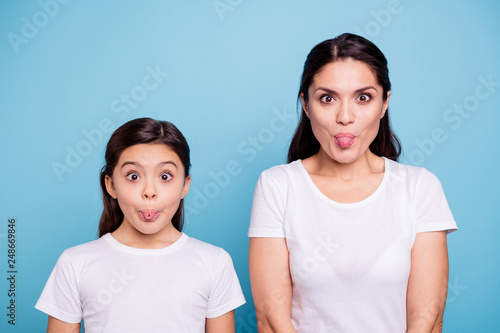 Close up photo beautiful two people brown haired mom little daughter friends look silly eyes opened tongue out of mouth playing fooling around wear white t-shirts isolated bright blue background