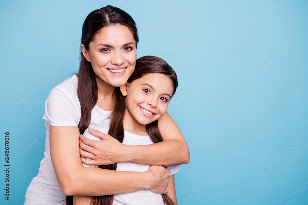Close up photo pretty two people brown haired mum small little daughter best friends stand hugging piggy back lovely nice free time rejoice wearing white t-shirts isolated on bright blue background Close up photo pretty two people brown haired mum small little daughter best friends stand hugging piggy back lovely nice free time rejoice wearing white t-shirts isolated on bright blue background