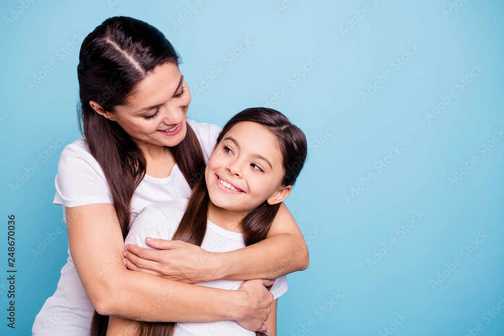 Close up photo pretty two people brown haired mum small little daughter missed glad see each other stand hugging piggy back nice rejoice wearing white t-shirts isolated on bright blue background Close up photo pretty two people brown haired mum small little daughter missed glad see each other stand hugging piggy back nice rejoice wearing white t-shirts isolated on bright blue background