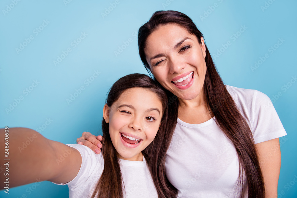 Close up photo cheer beautiful two people brown haired mum mom small little daughter make take selfies mouth laugh laughter flirty wink wear white t-shirts isolated bright blue background Close up photo cheer beautiful two people brown haired mum mom small little daughter make take selfies mouth laugh laughter flirty wink wear white t-shirts isolated bright blue background
