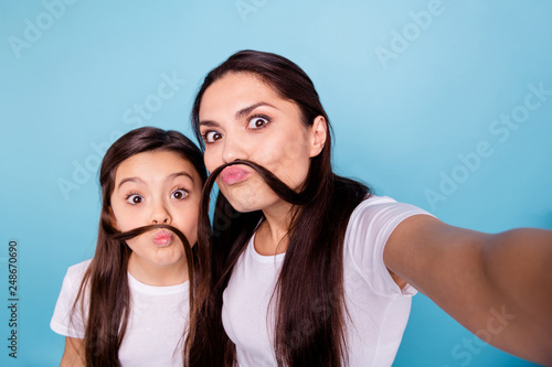 Close up photo amazing beautiful two people brown haired mom small little daughter make take selfies make moustache with curls pretend guy man male wear white t-shirts isolated bright blue background
