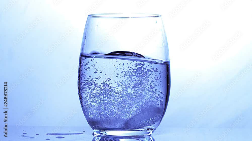 Tablets Falling into a Glass of Water against Blue Background, Slow Motion Tablets Falling into a Glass of Water against Blue Background, Slow Motion