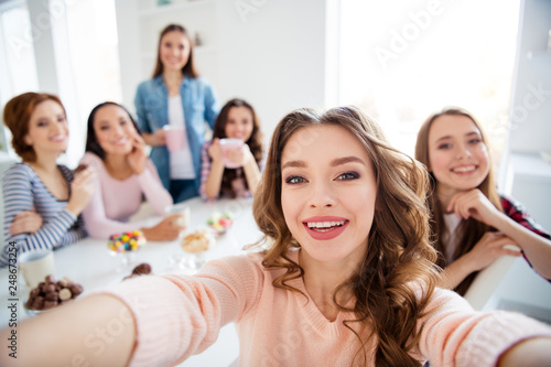 Close up portrait amazing beautiful she her diversity ladies sit round big white table in bright kitchen hold cups hot beverage glad make take selfies girls day night holiday indoors