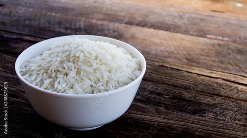 Dry rice in a white cup with grass flowers on a wooden background in dark tones.