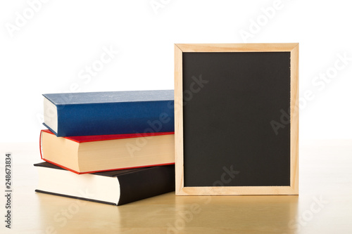Empty, blank, black chalkboard with stack of books on brown wooden desk over white
