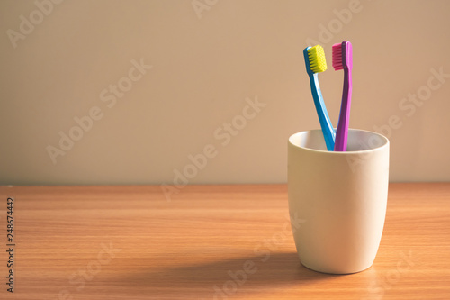 Couple toothbrush in white glass against wooden table © Eakawat