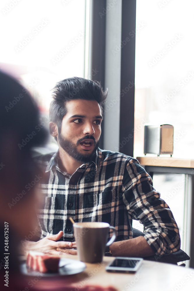 A stylish man with dark hair and a beard sitting at a table in a bright cafe near the window in front of the girl. cake and people in cafe concept. A stylish man with dark hair and a beard sitting at a table in a bright cafe near the window in front of the girl. cake and people in cafe concept.