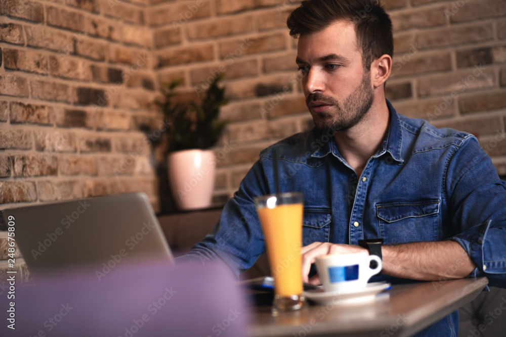 Young man sitting at cafe and working on laptop, casual businessman looking at computer. Young man sitting at cafe and working on laptop, casual businessman looking at computer.