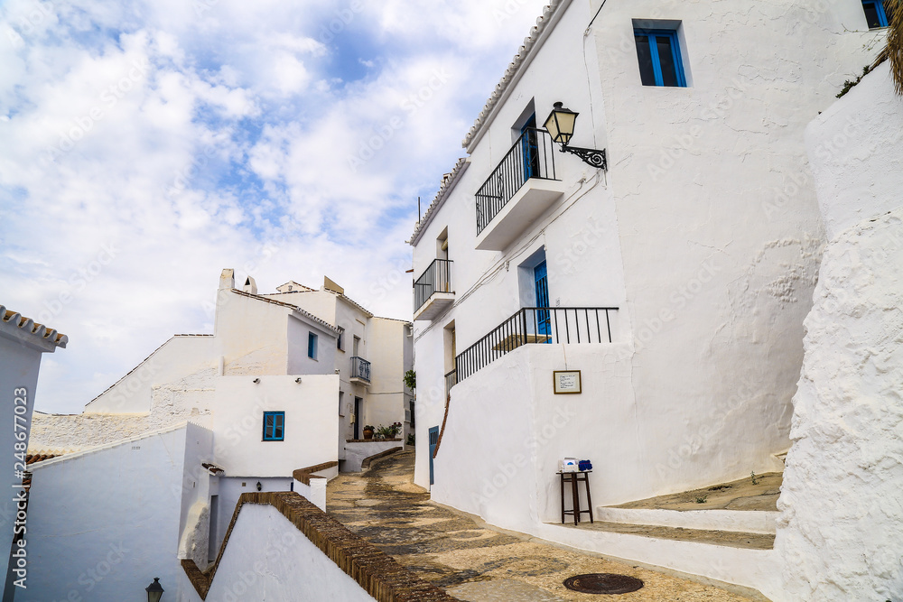 Stunning traditional architecture with white houses with blue windows and a small alley lane between under a sunny sky in frigiliana in spain