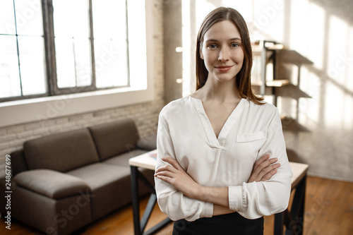 Nice cheerful businesswoman pose on camera. She stand alone in room. Empty. Daylight.