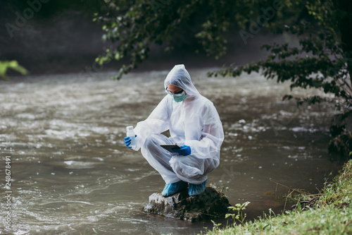 Scientist in protective suite taking water samples from the river.
