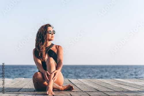 Pretty pan asian woman relaxing on the pier near sea in black swimsuit.