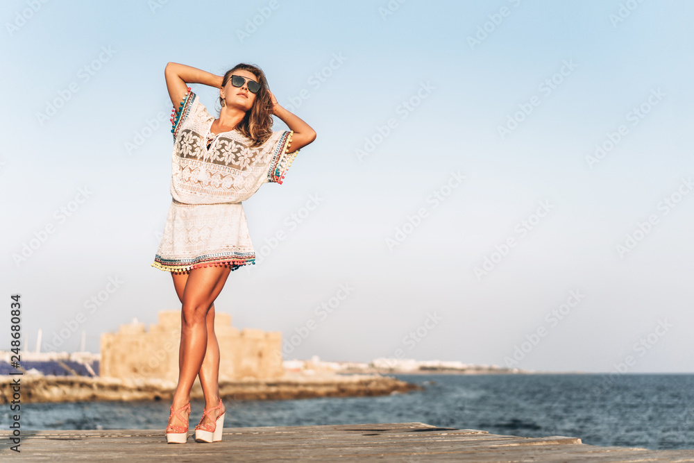 Pretty young woman in white pareo relaxing on pier near sea Pretty young woman in white pareo relaxing on pier near sea