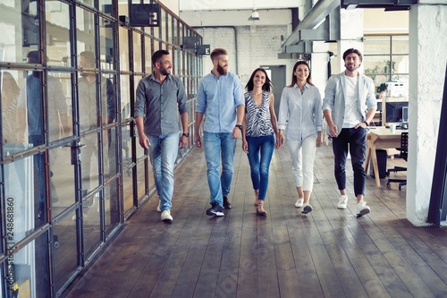 On the way to business meeting. Full length of young modern people in smart casual wear having a discussion while walking through the office. © opolja