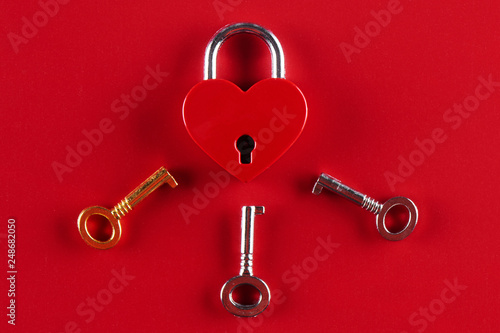 The concept of female infidelity. A heart shaped lock and three keys to it on a red background.