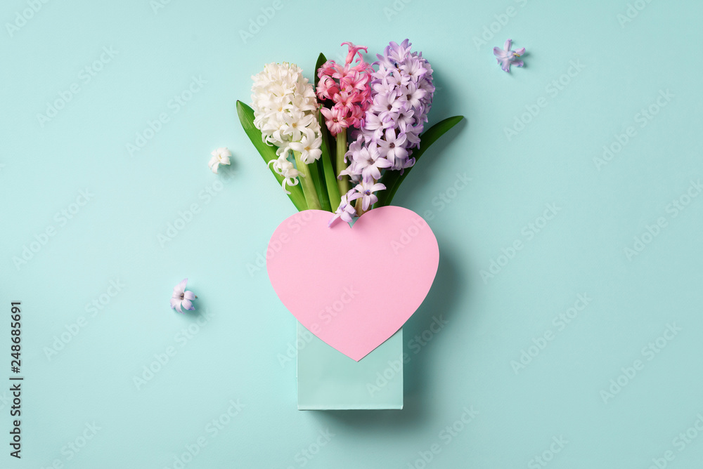 Spring hyacinth flowers in shopping bag, pink paper heart on blue punchy pastel background. Banner with copy space. Spring, summer or garden concept. Creative layout. Top view, flat lay.
