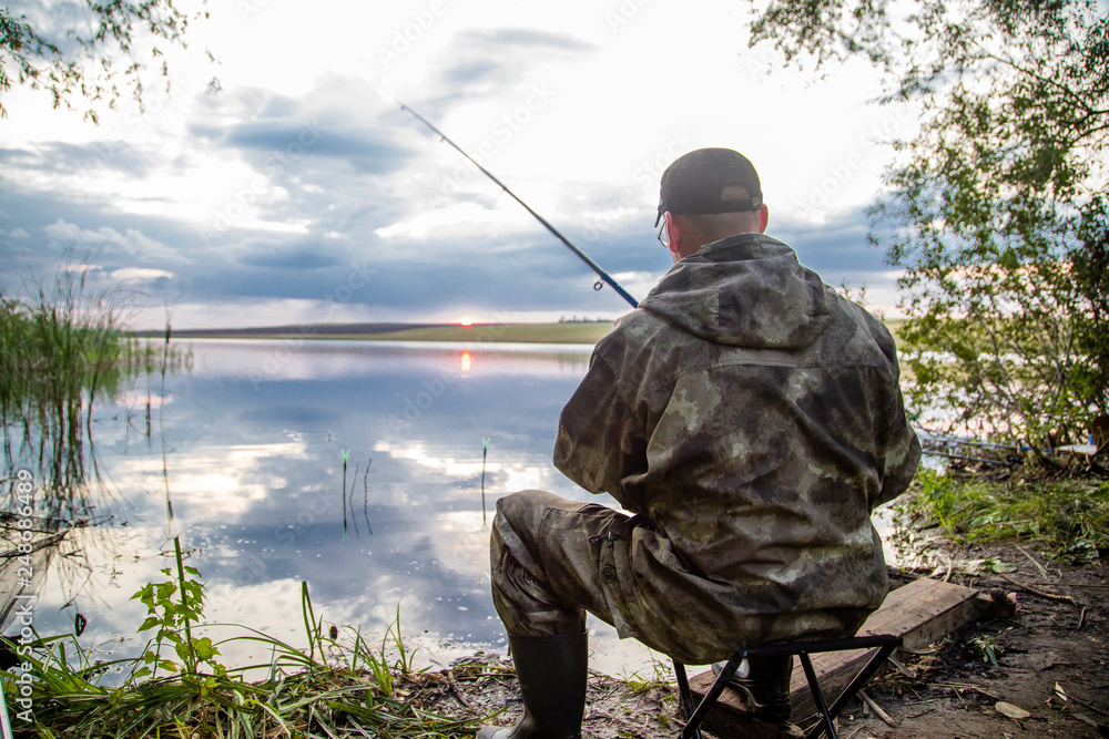 male fisherman sitting with a fishing rod on the lake, view from the back male fisherman sitting with a fishing rod on the lake, view from the back