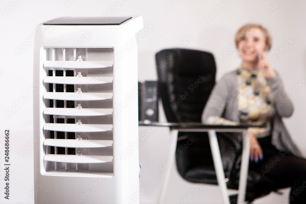 A woman works in an office with air conditioning. Air conditioning facilities. Outdoor air conditioning. Air purifier in the office. Humidifier. - obrazy, fototapety, plakaty 