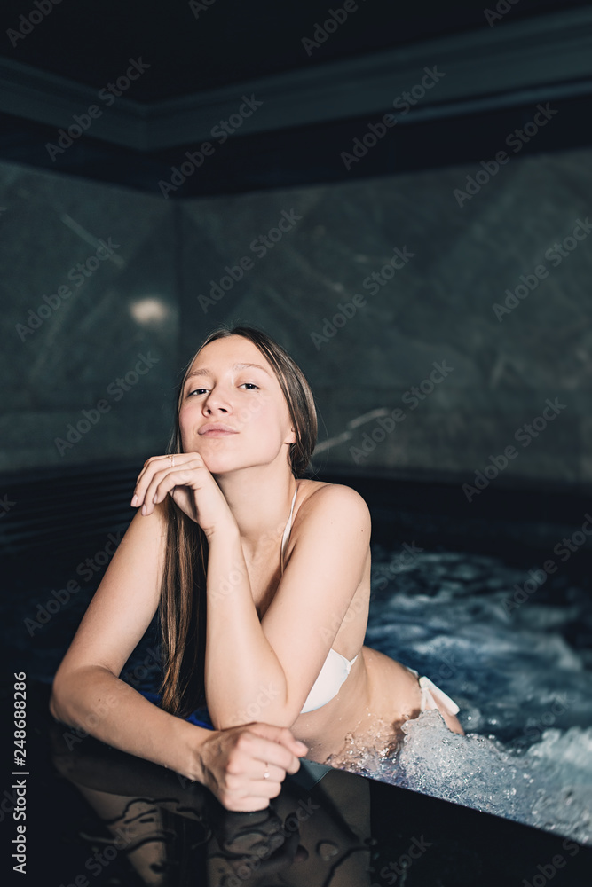 Sexy beautiful caucasian woman relaxing in a pool with jacuzzi. Dark room. Poor lighting