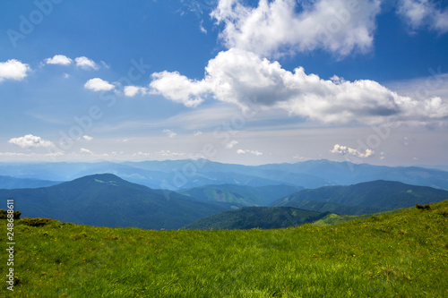 Green mountains panorama under blue sky on bright sunny day. Tourism and traveling concept, copy space background.