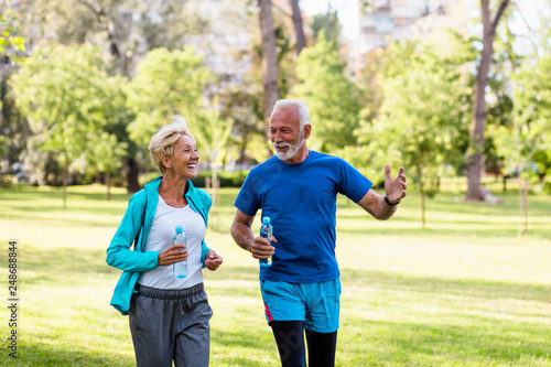 Happy senior couple jogging outdoors in park.