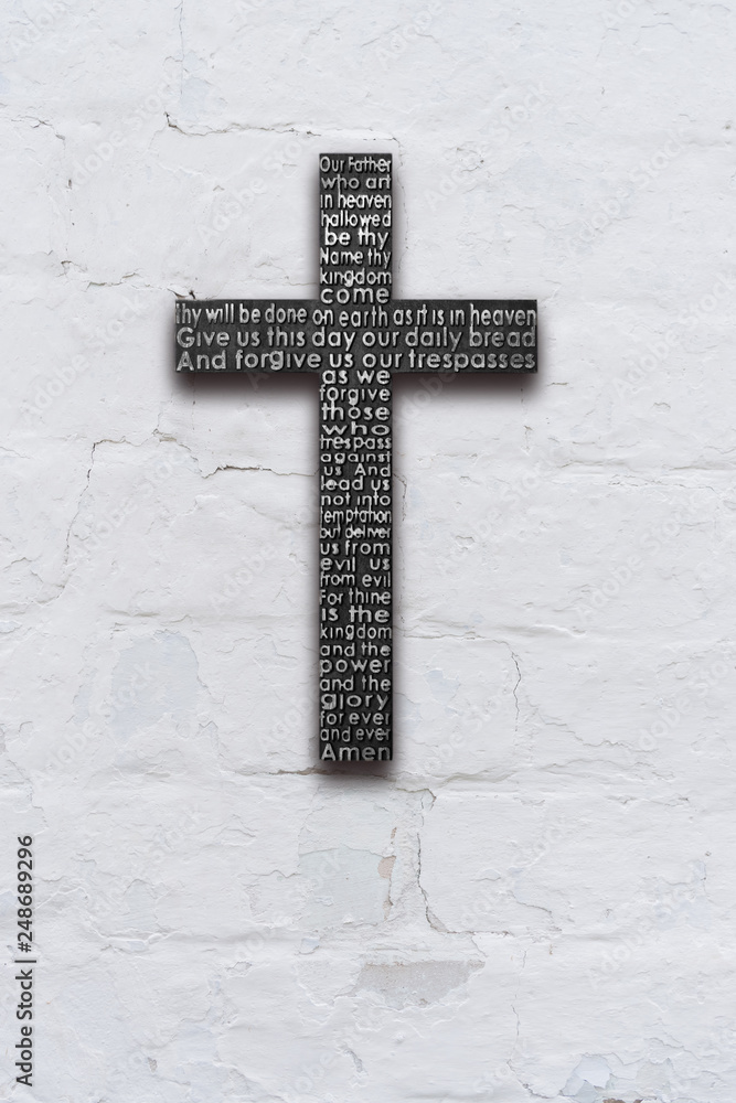 Black wooden cross with the Lord's prayer on white  brick wall with shabby stucco background