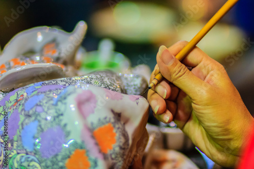 Close up hand of Thai woman artist during painting the masterpiece of Benjarong patterns, the famous thai 5- colored porcelain ceramic wares.