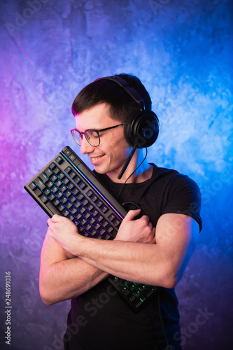 Professional Boy Gamer holding gaming keyboard over colorful pink and blue neon lit wall. Gaming gamers concept photo