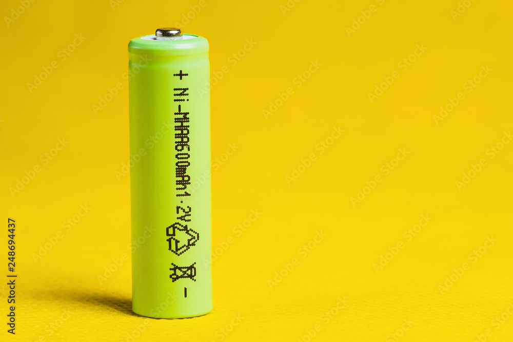Green battery Nickel metal hydride 1.2 volt, AA size, 600 mAH on yellow background. Close up. Green battery Nickel metal hydride 1.2 volt, AA size, 600 mAH on yellow background. Close up.