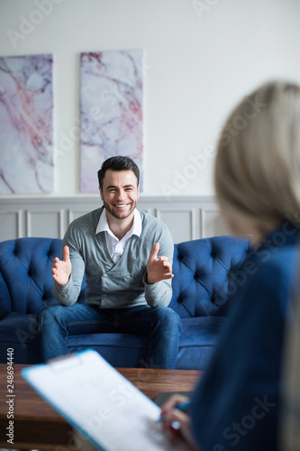 Man sits on the couch smiling and talking to a psychologist consultant.