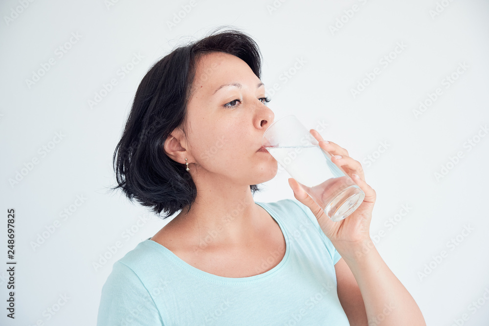 Happy beautiful young woman drinking water. Smiling caucasian female model holding transparent glass in her hand. Closeup. Focus on the arm Happy beautiful young woman drinking water. Smiling caucasian female model holding transparent glass in her hand. Closeup. Focus on the arm