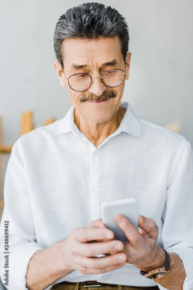cheerful senior man in glasses looking at smartphone at home cheerful senior man in glasses looking at smartphone at home