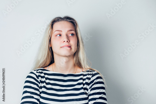 Close up indoor portrait of young dissatisfied woman biting lower lips on white background with copy space.