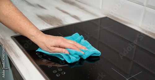 A woman's hand with a blue microfiber cloth rubs a glass ceramic stove in the kitchen.