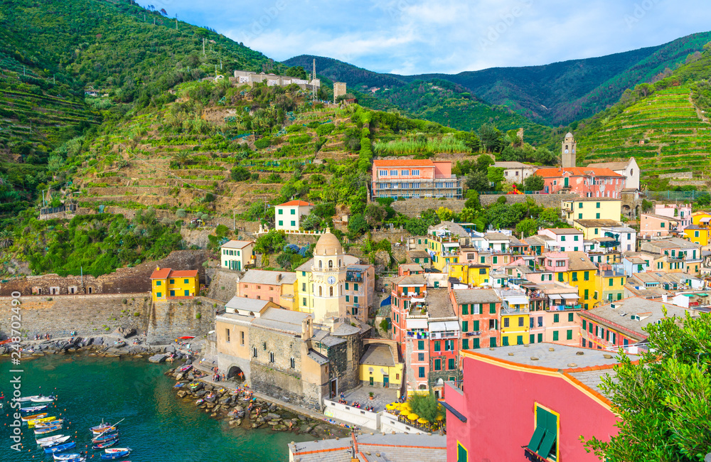 Top view of marina harbor with boats, Chiesa di Santa Margherita church, green hills and typical colorful buildings houses in Vernazza village, National park Cinque Terre, La Spezia, Liguria, Italy