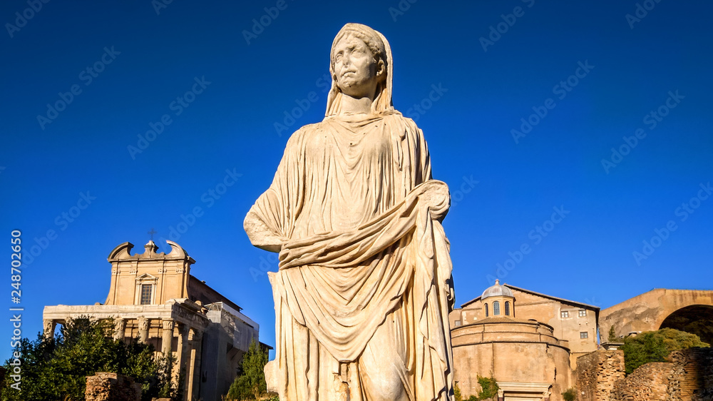 Ancient and weathered statue of a woman with the Roman Forum ruins in background in Rome, Italy