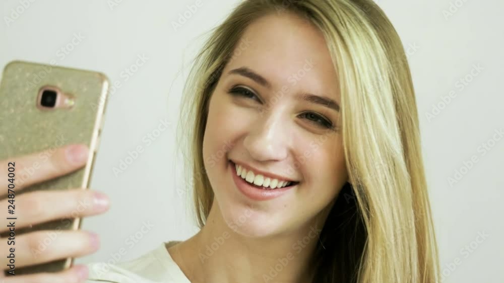 Beautiful blonde woman looking at her cell phone and taking a selfie in a modern cafe. 4K