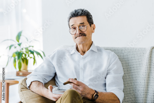 senior man with mustache holding sigar and ashtray in hands photo