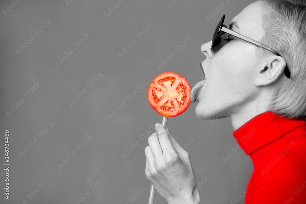 Hot beautiful blond woman model  eating tomato, black and white with red clothes and tomato slice - obrazy, fototapety, plakaty 
