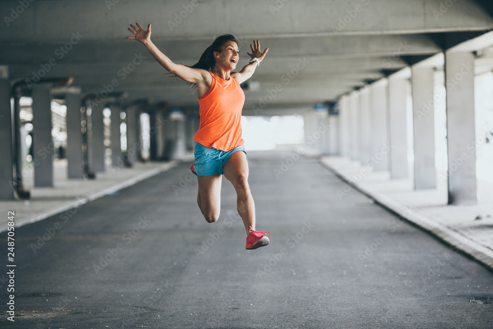 A young female runner jumps on the street, expressing positive emotion. She made her goal of the day. Fitness and workout concept.	